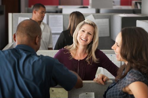 Three happy employees sit around a cubicle talking