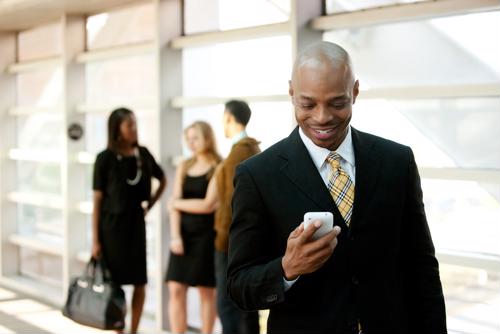 A businessman looks happily at his phone with three coworkers talking behind him