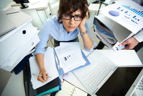 An employee looks stressed with papers and work strewn across her desk